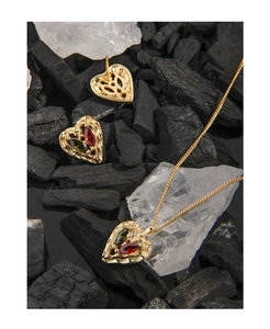 Macro detail of heart jewelry set with red and green gems on dark charcoal and white stone