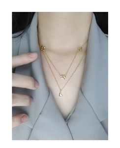 Detail of double-layer gold necklace featuring a floral charm and small heart pendant