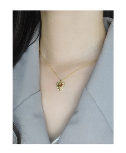 Detail of a heart pendant necklace with red and green inlay on a model in a gray suit