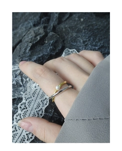 Detail of a minimalist double-layered cross ring with a small pearl in gold and silver
