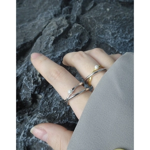 Double-layered crossed pearl rings in silver and gold, worn on hand against stone background