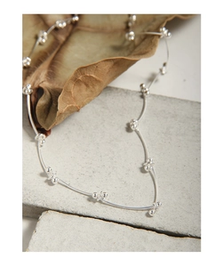 Detail of minimalist S925 sterling silver segmented chain on natural stone and leaf