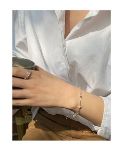 Minimalist silver chain bracelet with beads and pearl ring worn in a chic lifestyle setting