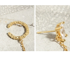 Macro detail of gold S925 sterling silver ear cuff and zircon stud linked by chain
