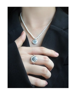 Detail of silver smiley face ring and pearl necklace with pink zircon eyes on black suit