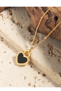 Gros plan détaillé du collier coeur doré avec incrustation noire sur surface en pierre