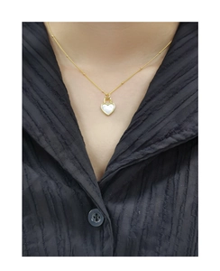 Détail d'un pendentif cœur doré avec nacre blanche sur une chaîne à fines perles dorées
