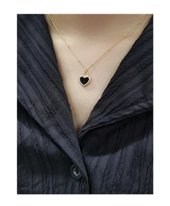 Détail du pendentif cœur doré avec incrustation noire porté par un mannequin sur tissu