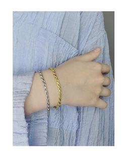 Close-up of elegant gold and silver twisted rope chains worn by a model on a blue background