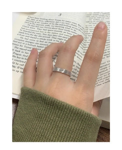 Gros plan sur une bague coeur en argent mat S925 portée par un mannequin sur un livre