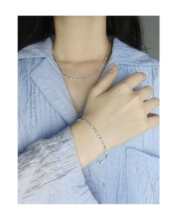 Detailed view of silver necklace and bracelet set with faceted shimmering texture on model