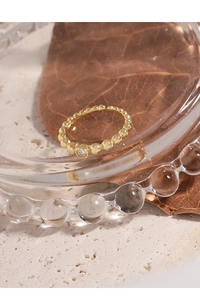 Detailed shot of golden beaded ring with micro-set zircon on textured stone surface