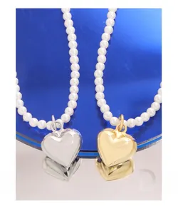 Détail macro de pendentifs cœurs or et argent avec perles blanches rondes sur socle miroir