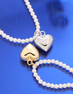 Gros plan de pendentifs en cœur or et argent sur des colliers de perles blanches