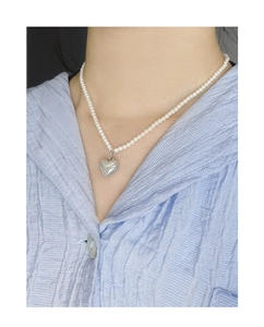 Vue détaillée du pendentif cœur argenté sur un collier de perles blanches