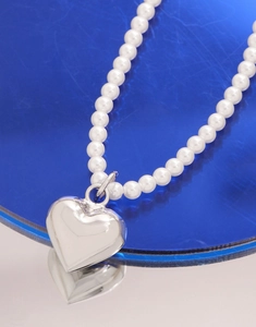 Vue macro d'un pendentif cœur en argent et collier de perles sur support bleu poli