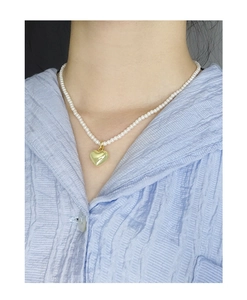 Vue détaillée d'un collier de perles fines avec pendentif cœur doré sur un mannequin