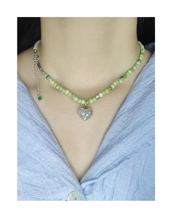 Detail of beaded necklace featuring green pearls and polished silver heart pendant