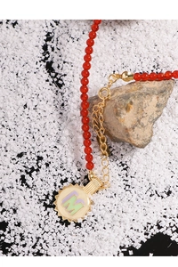 Detail of red beaded necklace with golden M pendant on natural stone base