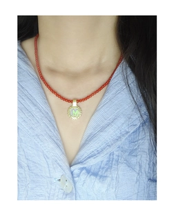 Detail of red agate beaded necklace with gold M-letter pendant on model's neck