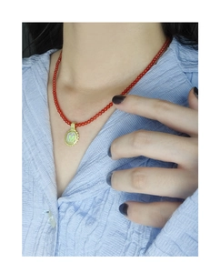 Close-up of red beaded necklace with a gold M pendant worn on a blue striped shirt