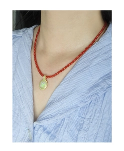 Close-up of red beaded necklace with golden M letter pendant on a model wearing blue shirt