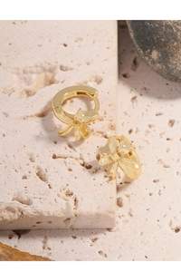 Macro shot of gold bow earrings on stone base showing the S925 sterling silver stamp