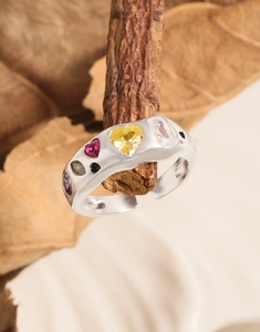 Detail shot of a silver adjustable ring featuring colorful heart-shaped zircon on a wood branch