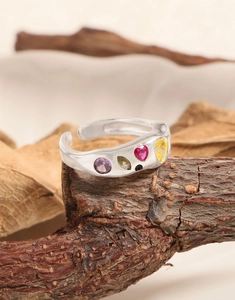 Macro shot of silver open ring with multi-color zircon stones on natural wood