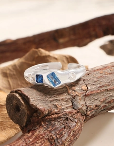 Detail of wavy S925 silver ring with blue gemstone and white zircon on wood