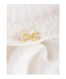 Close-up of geometric hexagonal gold studs with sparkling cubic zirconia on white fabric