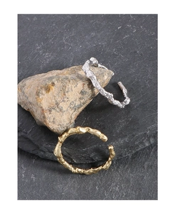 Detail of gold and silver open rings with irregular lava texture on dark stone surface