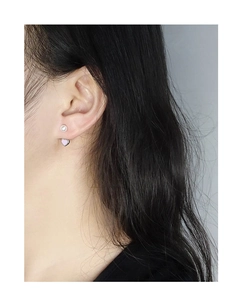 Détail d'un clou en perle argentée et d'une boucle d'oreille cœur violet clair sur l'oreille