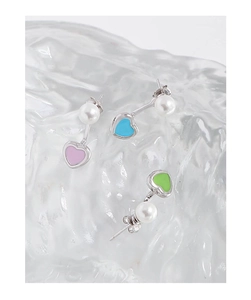 Vue macro de boucles d'oreilles cœur en émail coloré et perles sur décor de glace claire