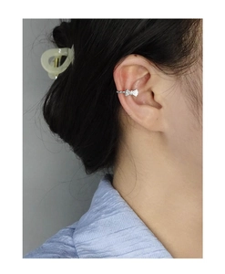 Detailed close-up of a silver bow ear cuff with zircon accents worn on the ear helix