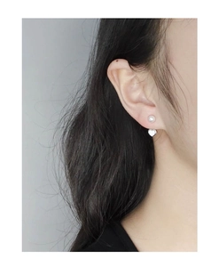Détail d'un clou d'oreille en perle avec cœur blanc porté par un mannequin
