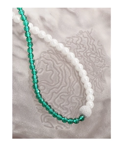 Detailed macro shot of asymmetrical green crystal and pearl beaded necklace with silver bead