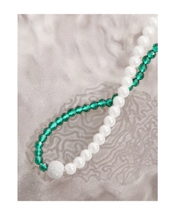 Macro detail of asymmetric necklace featuring green crystals and white lustrous pearls