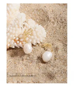 Detail of golden bow earrings with natural baroque pearls on beach sand and coral