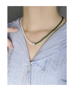 Close-up of asymmetric necklace with white pearls and green faceted beads on a model