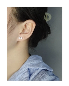 Close-up of sparkling silver bow earrings with pavé zircons worn on model ear