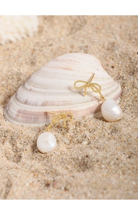 Close-up of golden bow earrings with natural baroque pearls on a beach background