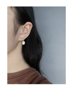 Close-up of bow knot earrings with natural baroque pearls worn by a model