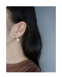 Detailed close-up of a golden bow and baroque pearl drop earring worn by a model