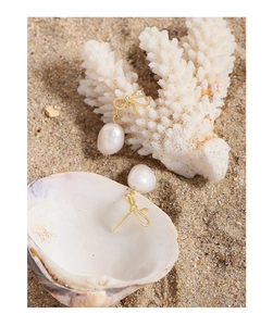 Elegant bowknot earrings with baroque pearls displayed on a natural coral beach background