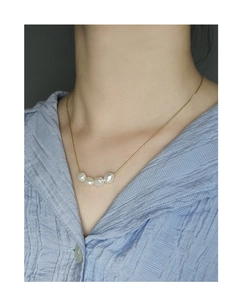 Close-up of four baroque pearls on a gold chain necklace worn by a model in a blue shirt
