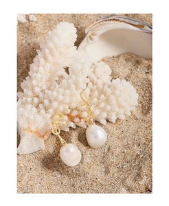 Baroque pearl drop earrings with golden bow detail on white coral and beach sand background