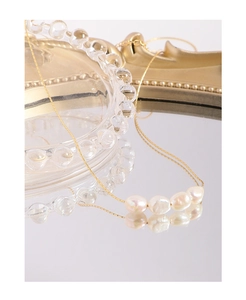 Close-up of five baroque pearls on a gold chain reflected on a mirror surface