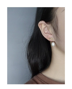 Detail of bow-shaped pearl stud earring on model with elegant gold metallic finish