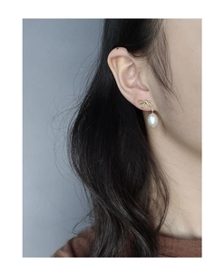 Detailed close-up of a golden bow stud earring with a hanging white baroque pearl drop